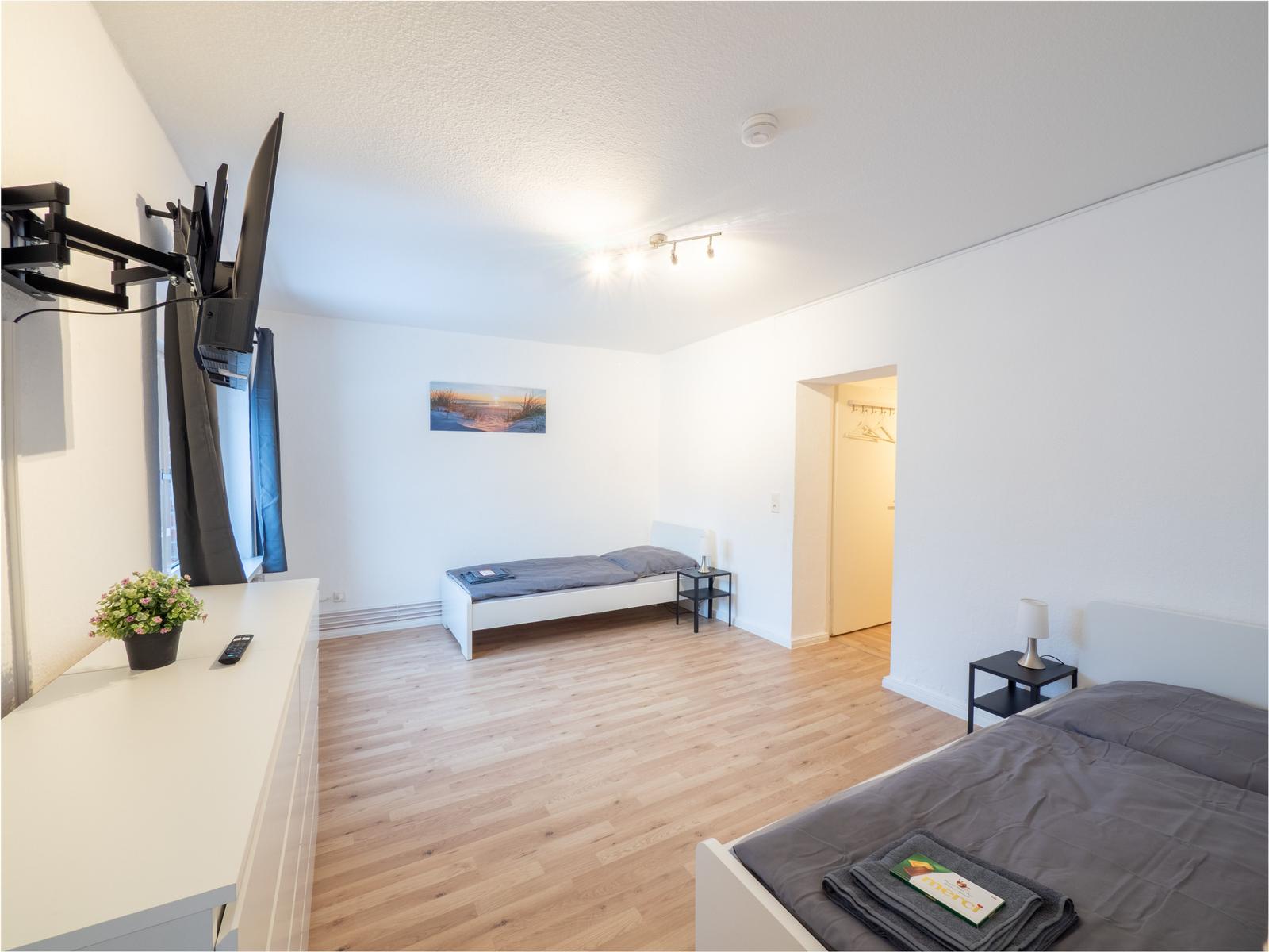 Zimmer mit zwei Betten, Holzboden und TV. Kleine Garderobe im Hintergrund.