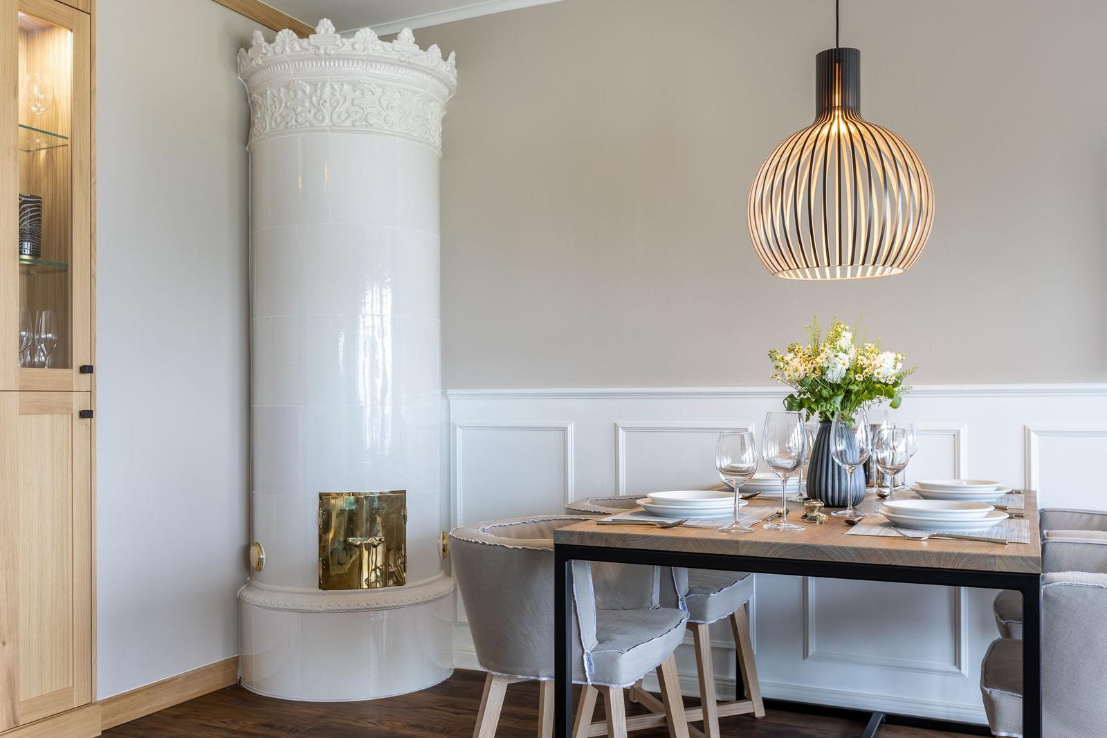 Esszimmer mit weißem Kachelofen, Holztisch und Lampe