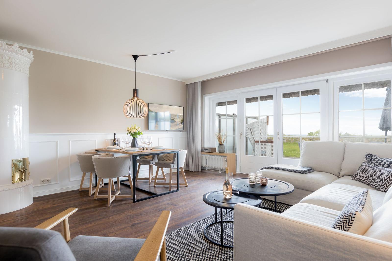 Wohn- und Essbereich mit Sofa, Tisch und Fernseher. Durchgang zur Terrasse mit Blick auf Grünfläche.