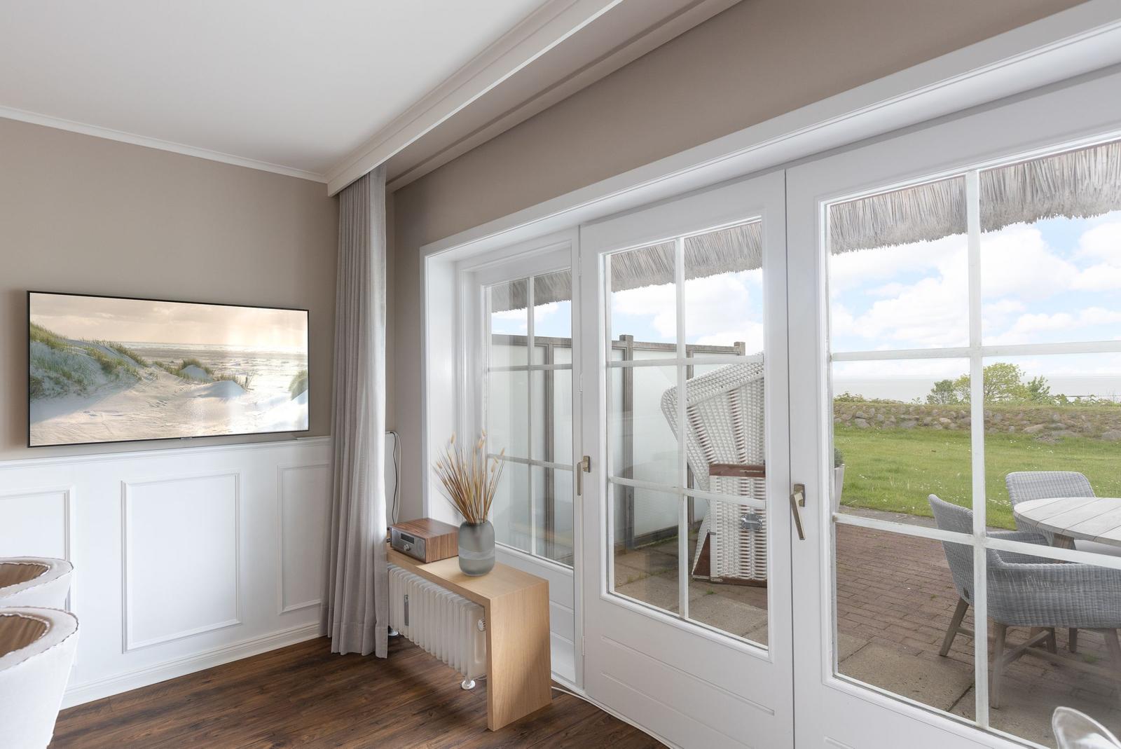 Wohnzimmer mit TV, Terrasse und Meerblick durch Glastüren.