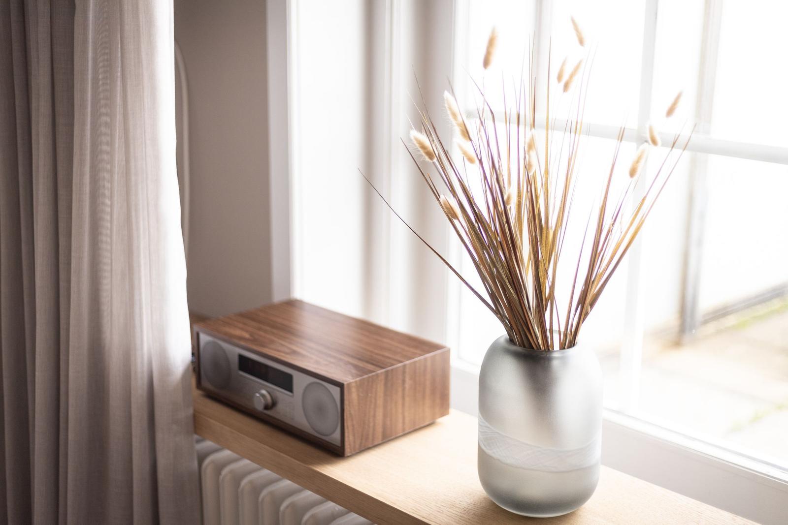 Auf einem Fensterbrett steht ein Radio und eine Vase mit getrockneten Pflanzen.