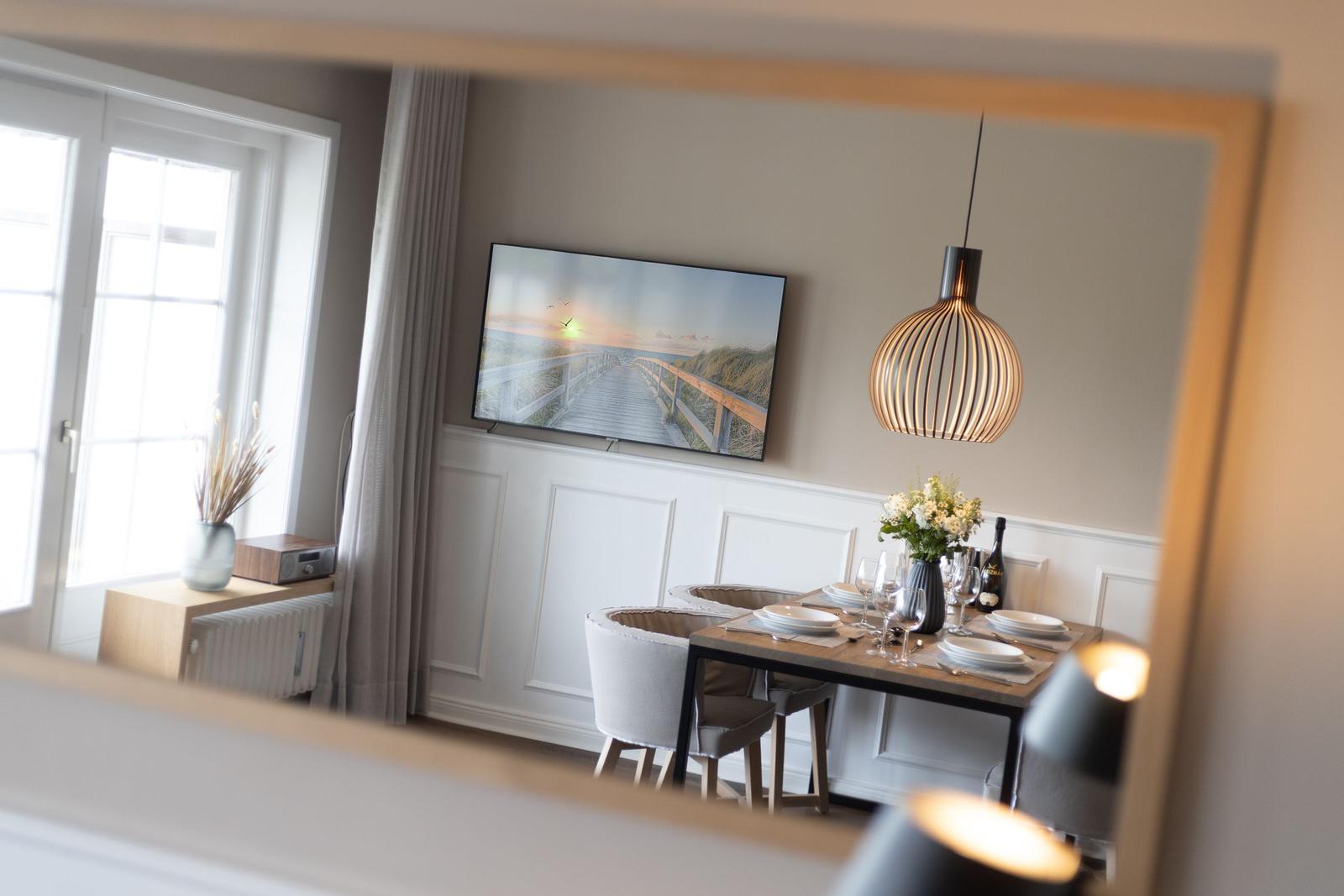 Esszimmer mit Tisch, Stühlen und Wandbild. Hängelampe und Fenster sichtbar.