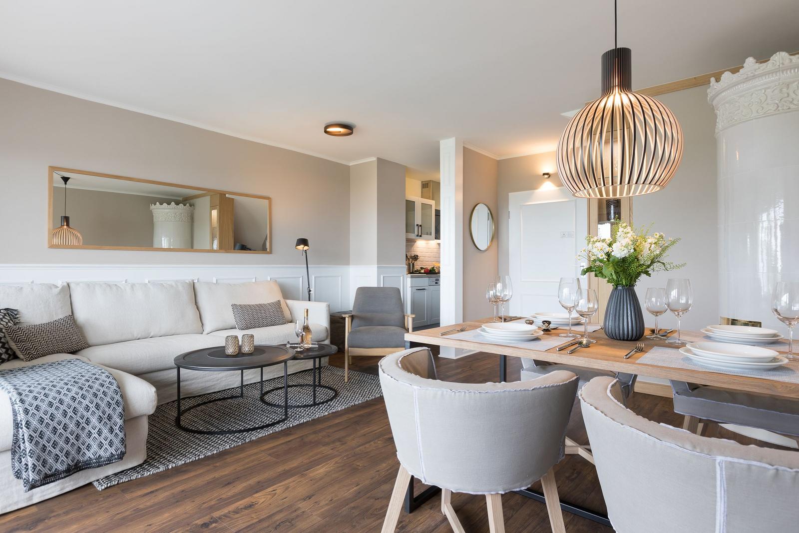 Wohn- und Essbereich mit Sofa, Tisch und Stühlen. Holzboden und moderne Beleuchtung.