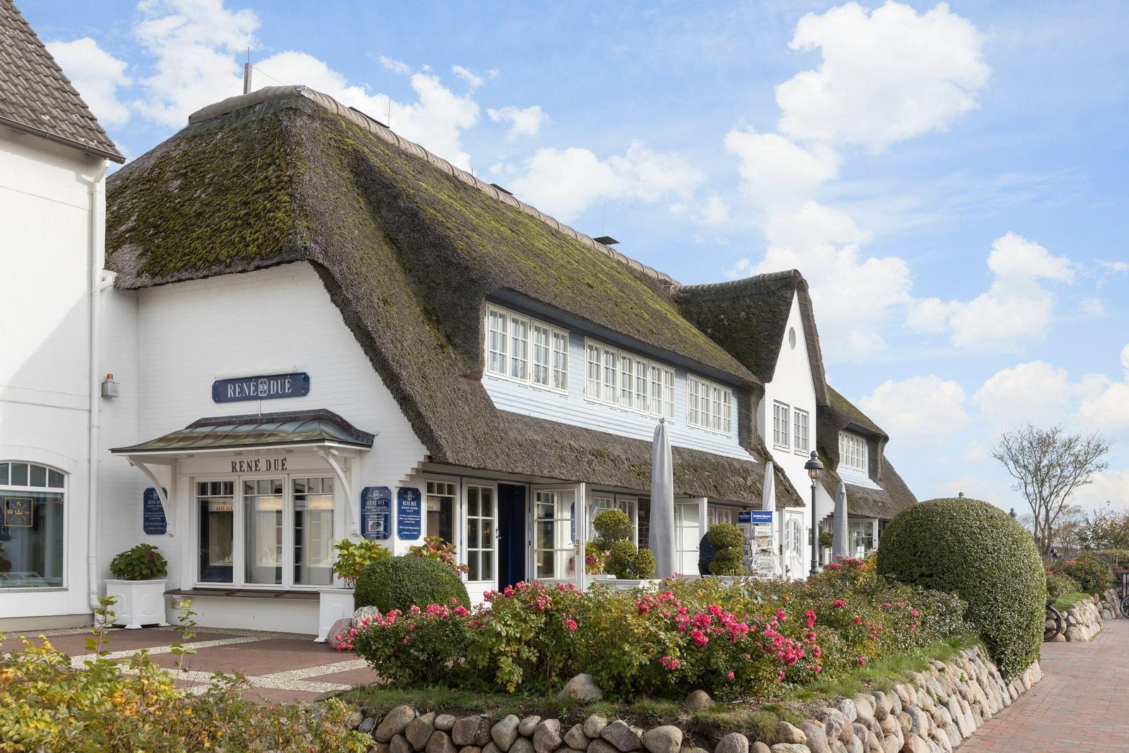 Weiße Villa mit Strohdach und Blumenbeet