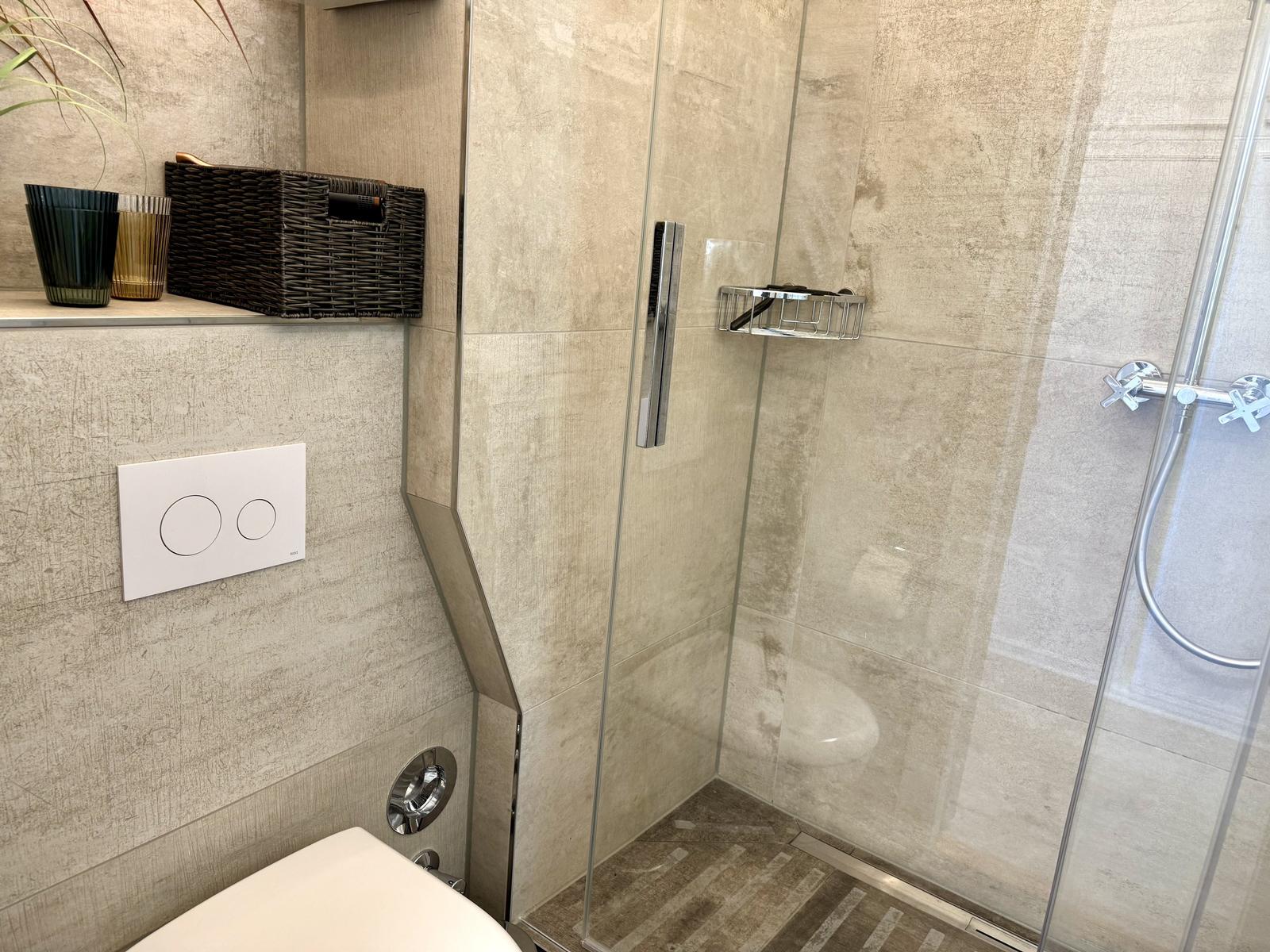 Duschkabine mit Glaswand, Toilette und Ablagefläche mit Korb und Vasen.