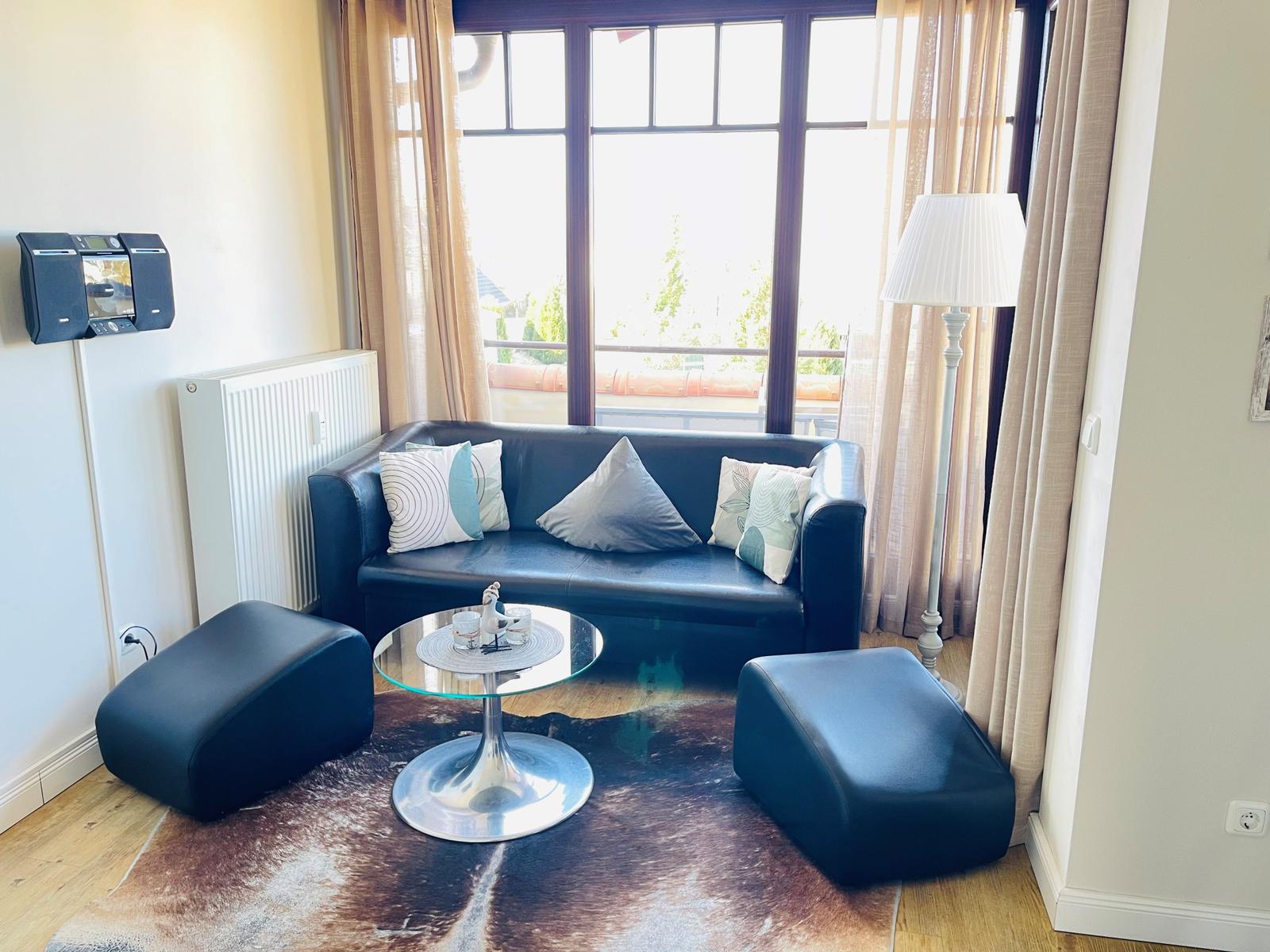 Ein Wohnzimmer mit Sofa, zwei Sitzkissen, Glas-Tisch und Balkon.