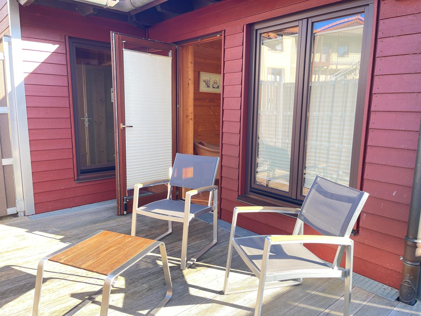 Terrasse mit zwei Stühlen und Tisch vor rotem Holzhaus mit offener Tür.