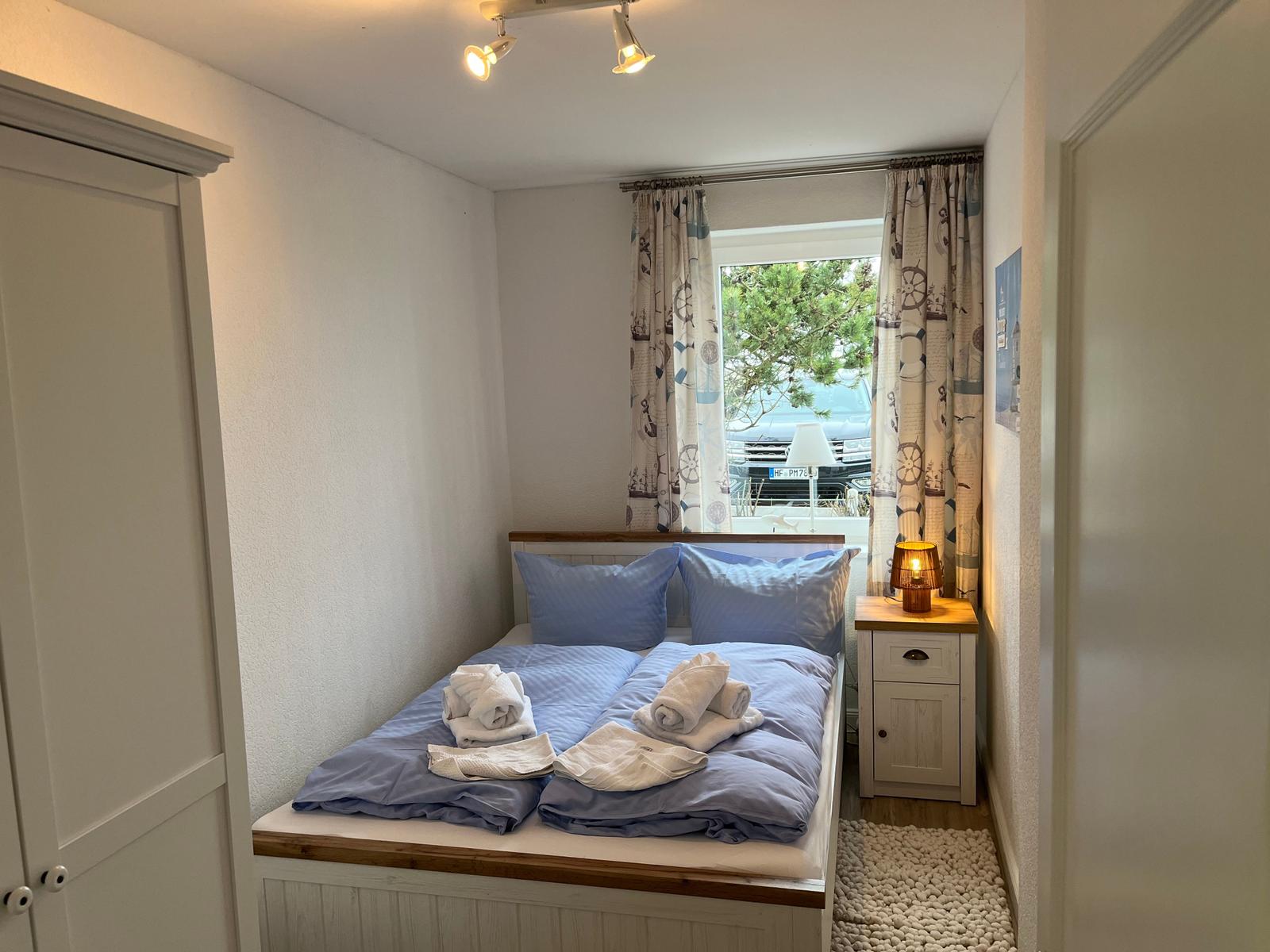 Schlafzimmer mit Bett, Nachttisch und Fenster mit Vorhängen.