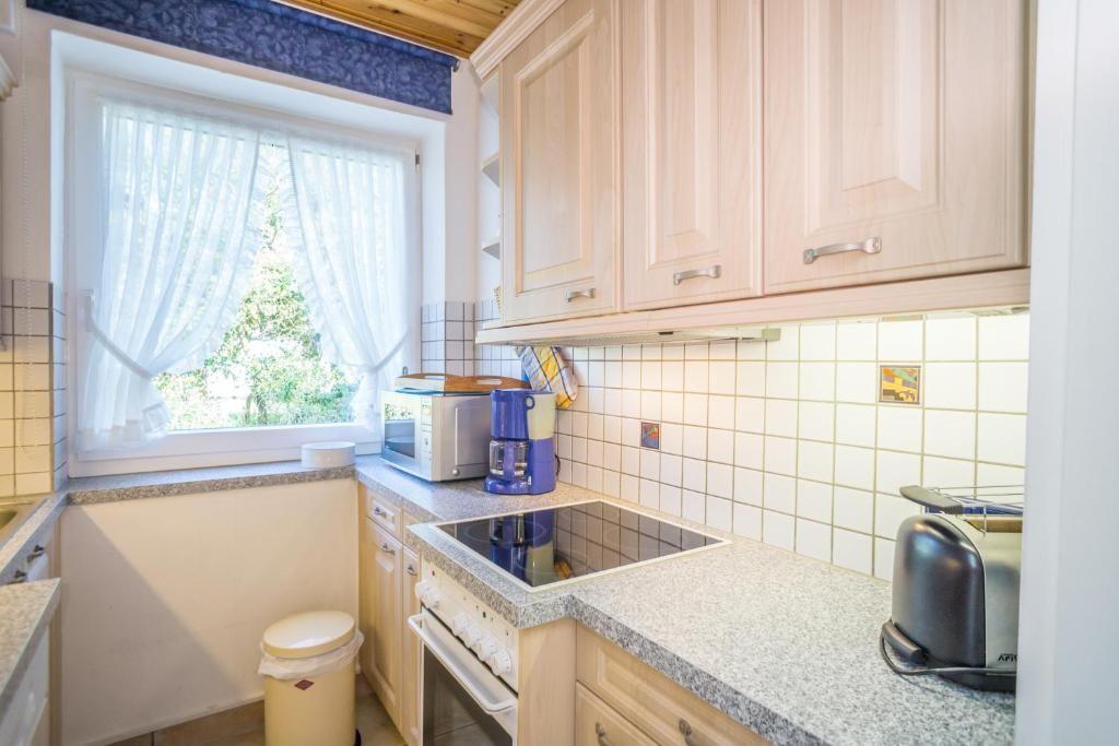 Küche mit Holzschränken, Arbeitsplatte und Fenster mit Vorhängen.