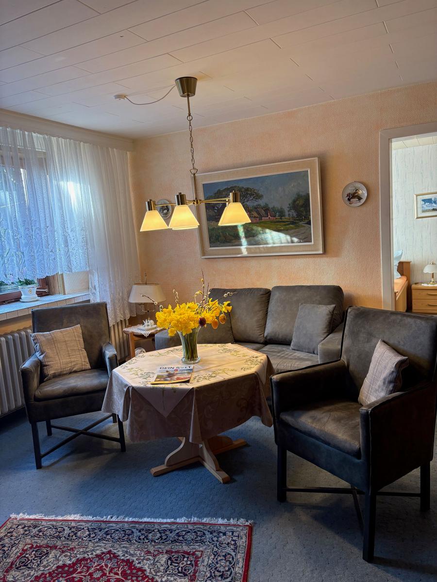 Wohnzimmer mit Sofa, zwei Sesseln, Tisch mit Blumen und Wandbild.