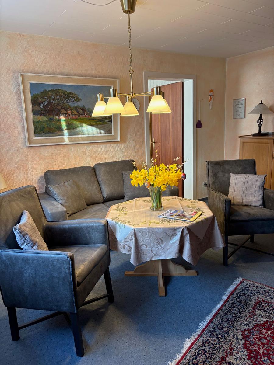 Wohnzimmer mit Sofa, zwei Sesseln, runden Tisch und Blumen.