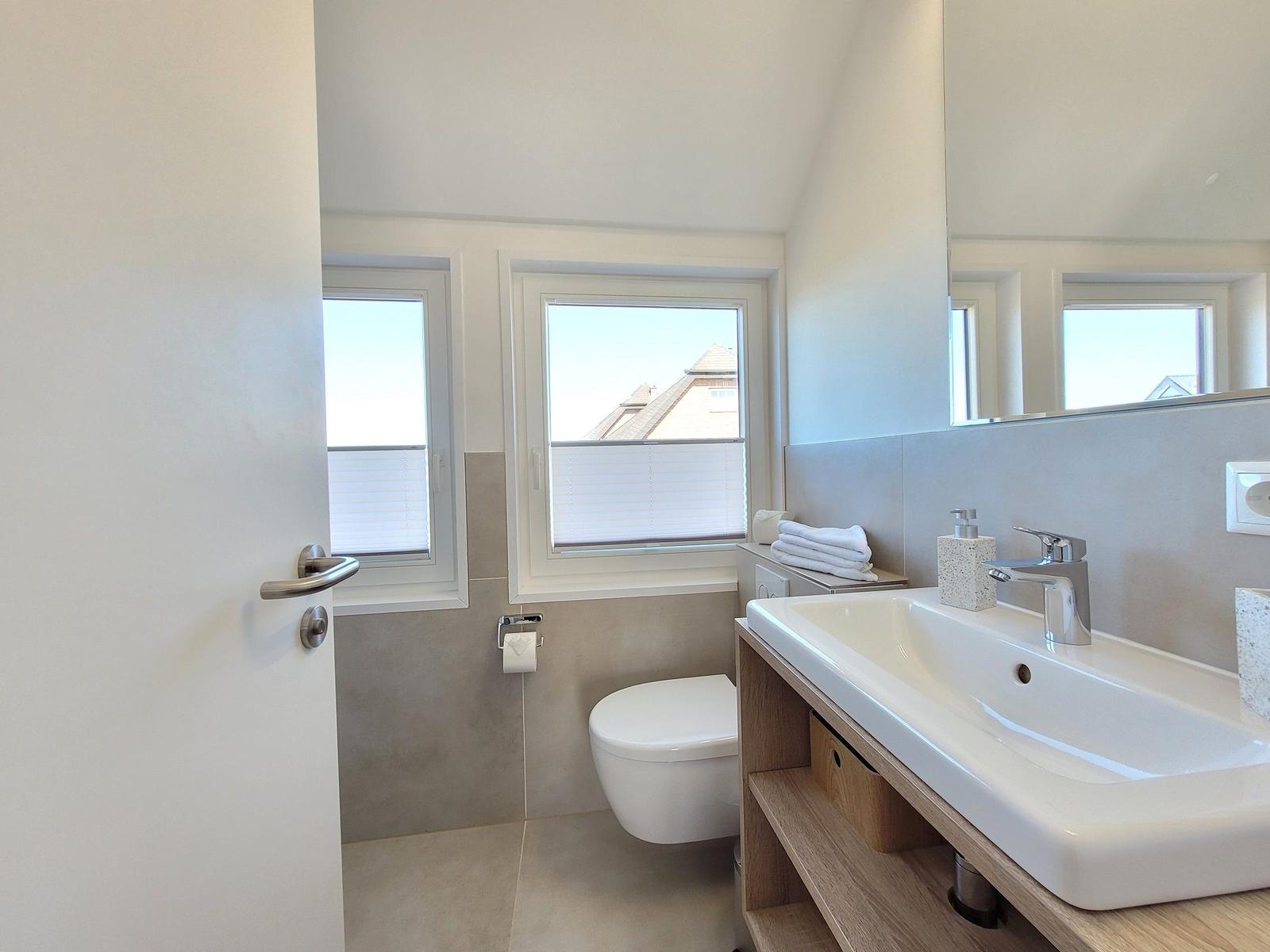 Badezimmer mit Waschbecken, Toilette und Fenstern.