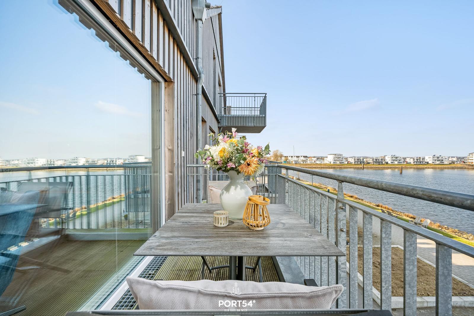 Terrasse mit Tisch, Blumen und Blick auf Wasser und Stadt.