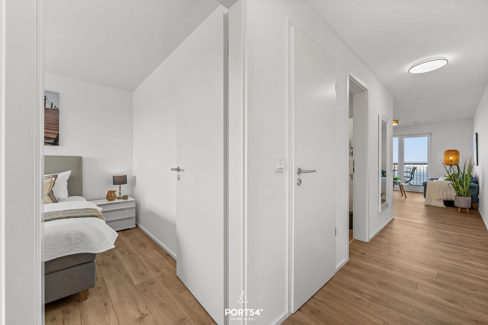Schlafzimmer mit Bett und Nachttisch. Flur mit Türen. Wohnbereich mit Balkon und Pflanze.