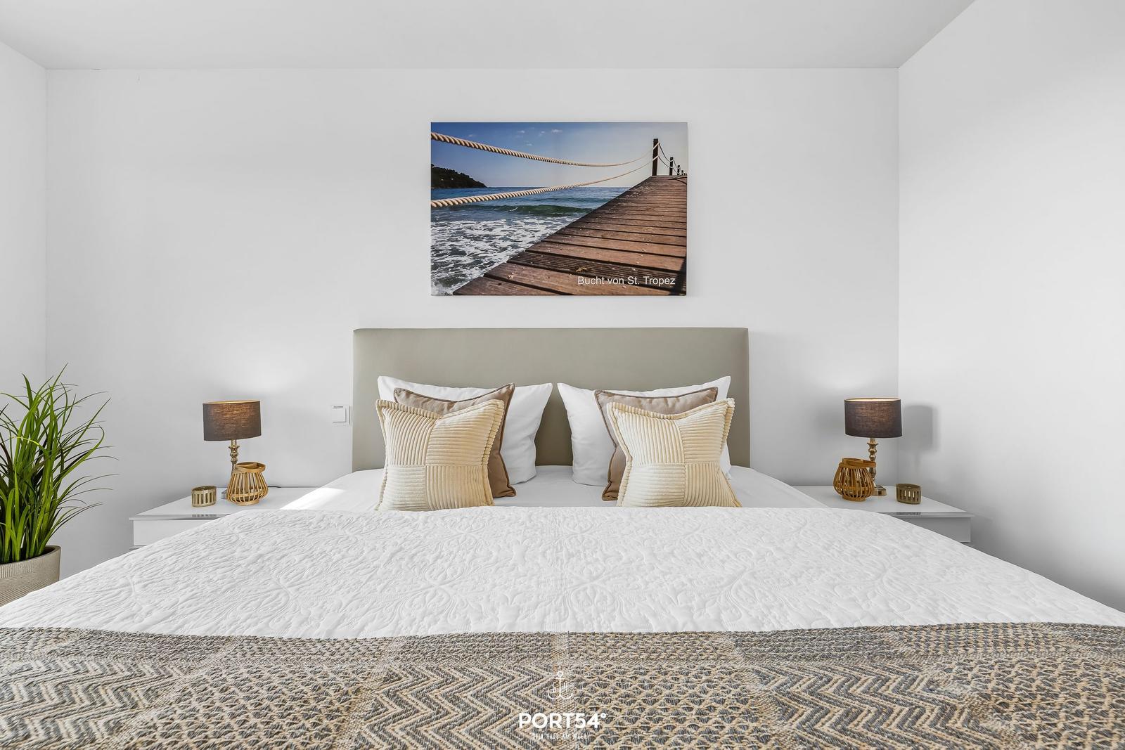 Schlafzimmer mit Bett, zwei Nachttischen und Wandbild von St. Tropez.