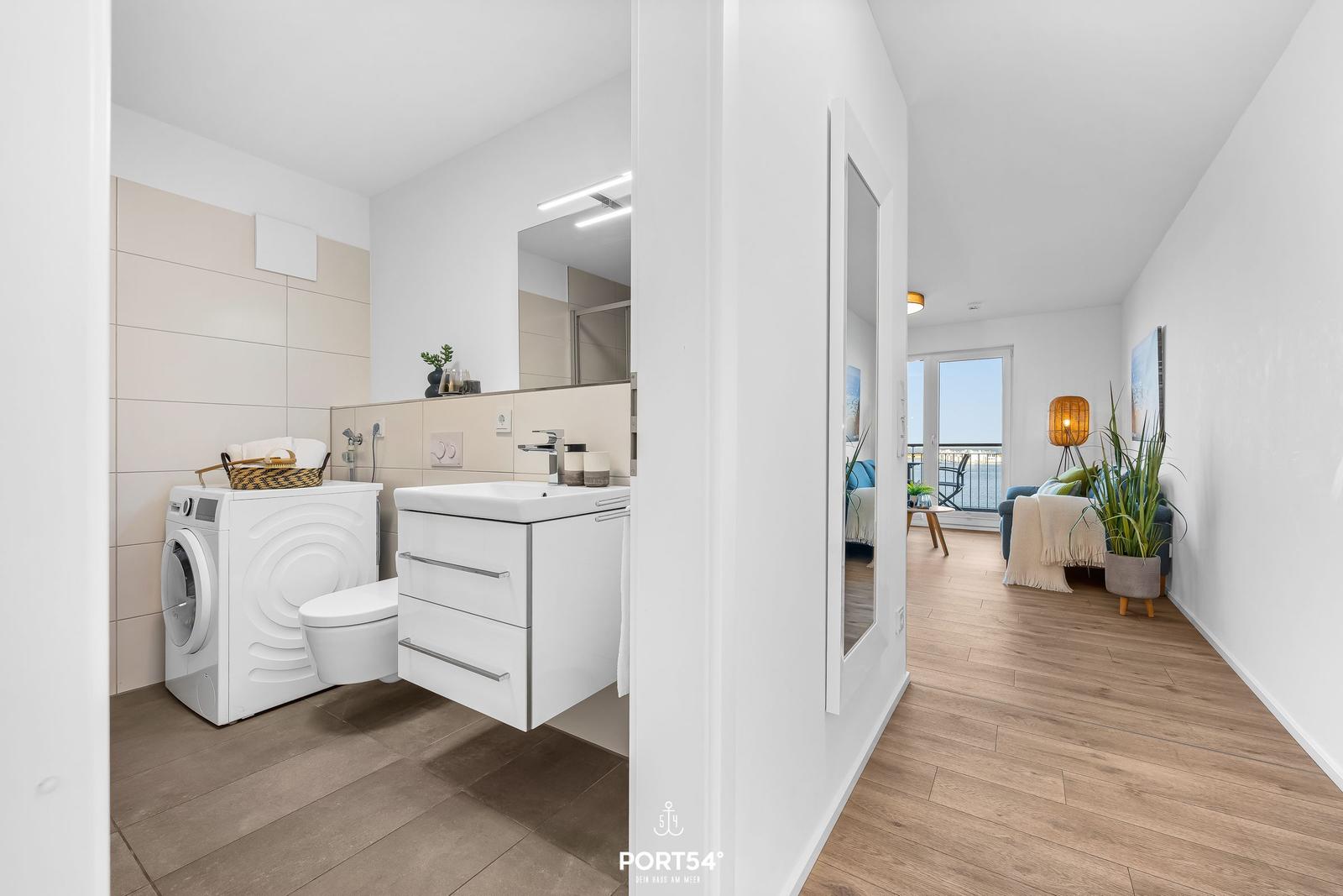 Badezimmer mit Waschmaschine und Spiegelschrank. Durchgang in Wohnbereich mit Balkon.
