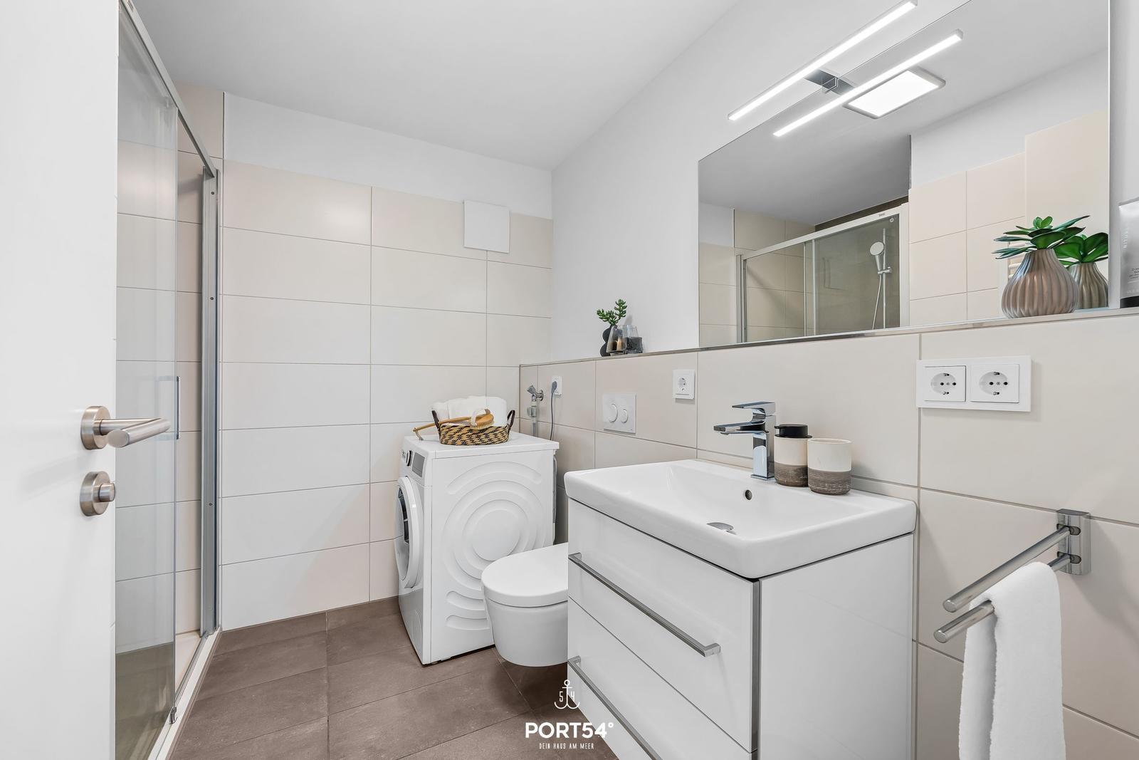 Badezimmer mit Dusche, Waschmaschine und Spiegel.