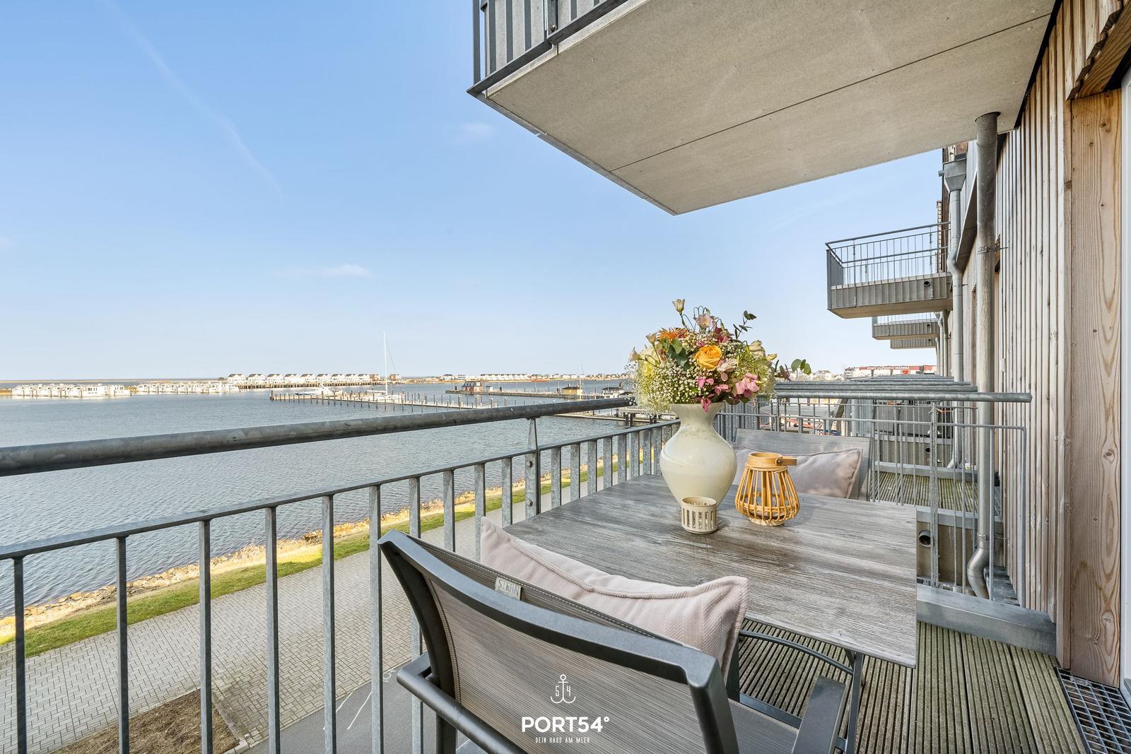 Terrasse mit Tisch und Stühlen, Blick auf Wasser und Steg.