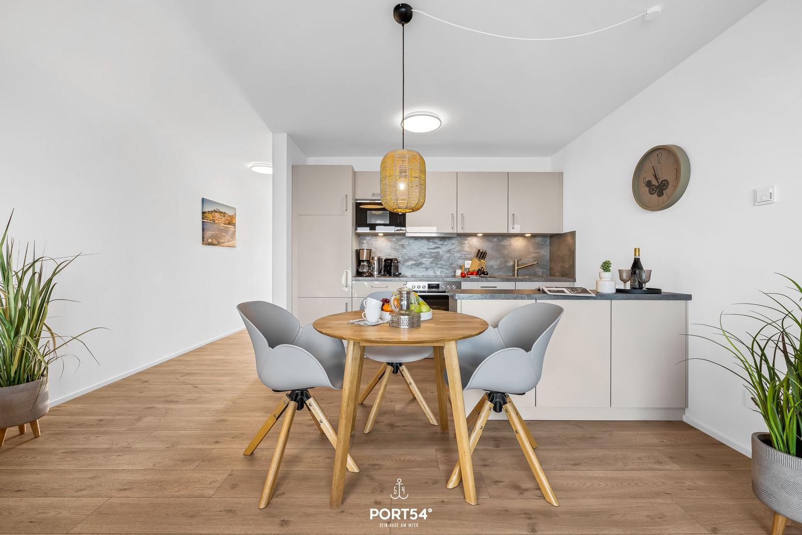 Küche mit Essbereich, Holztisch, graue Stühle und Pflanzen.