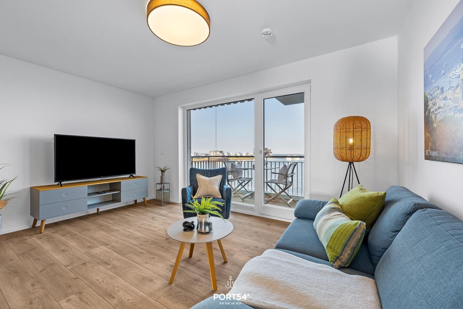 Wohnzimmer mit Sofa, Fernseher und Balkonansicht.