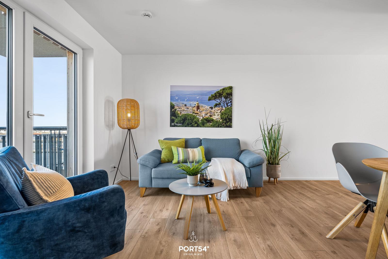 Wohnzimmer mit blauem Sofa, Holzboden und Blick auf Balkon.