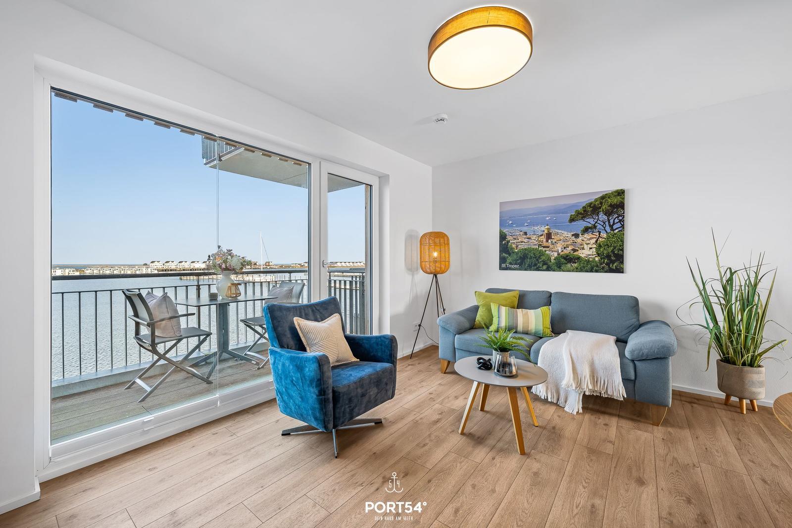 Wohnzimmer mit Blick auf den Hafen, blaues Sofa und Stuhl, Holzboden und Balkon.