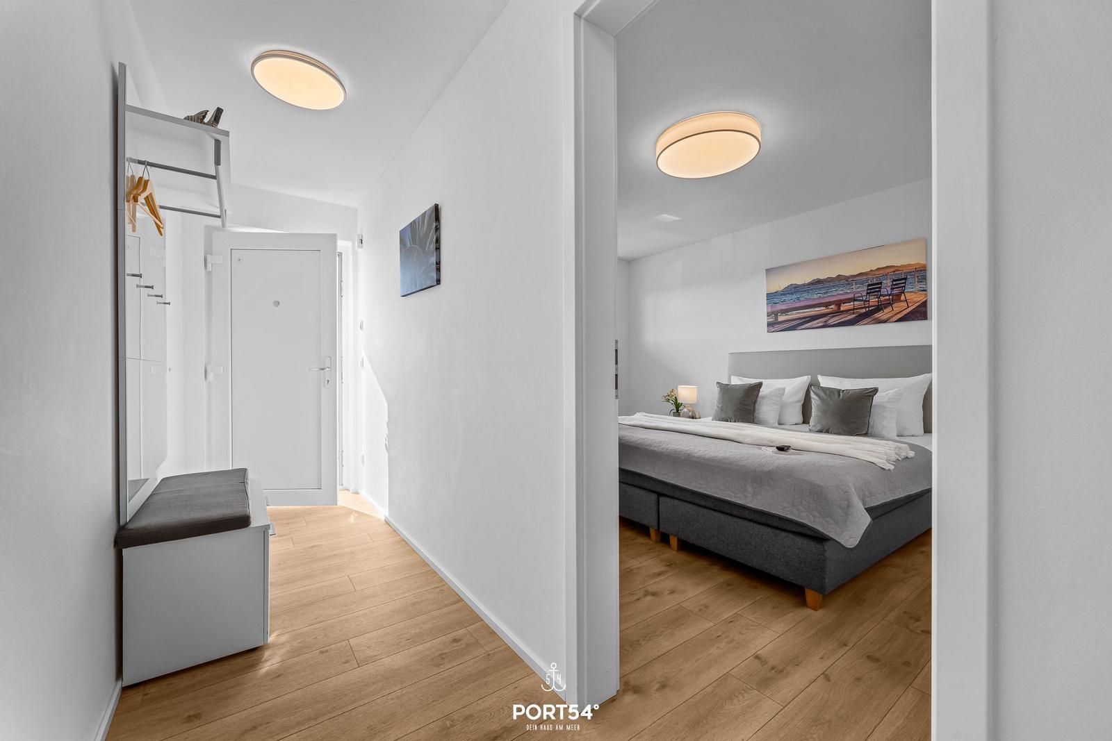 Schlafzimmer mit Bett und Wandbild. Flur mit Garderobe und Holzboden.