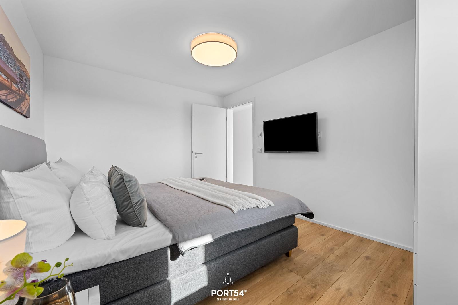 Schlafzimmer mit Bett, Fernseher und Holzboden.