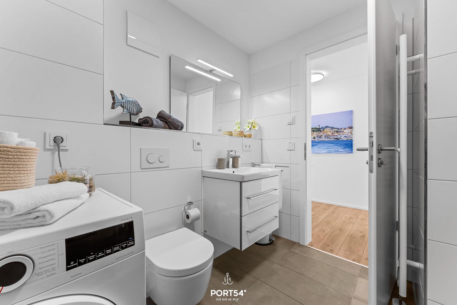 Badezimmer mit Waschmaschine, Spiegelschrank und Blick in Wohnbereich.