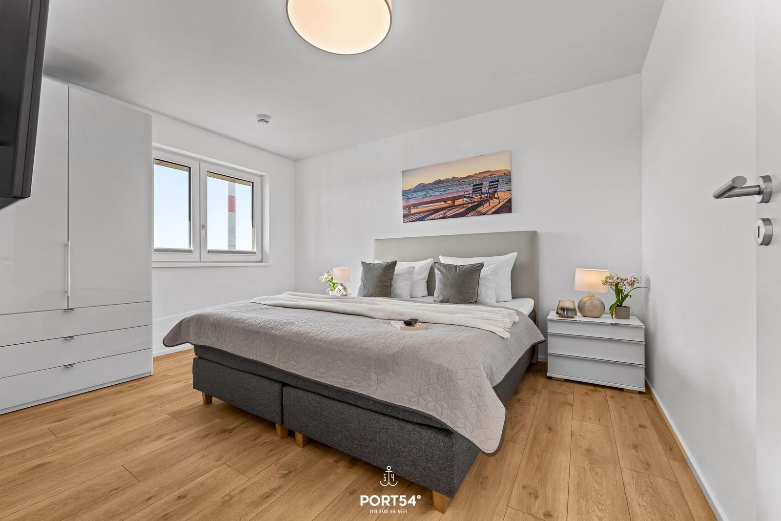 Schlafzimmer mit Bett, Nachttisch, Kleiderschrank und Fenster. Wandbild und Holzboden.