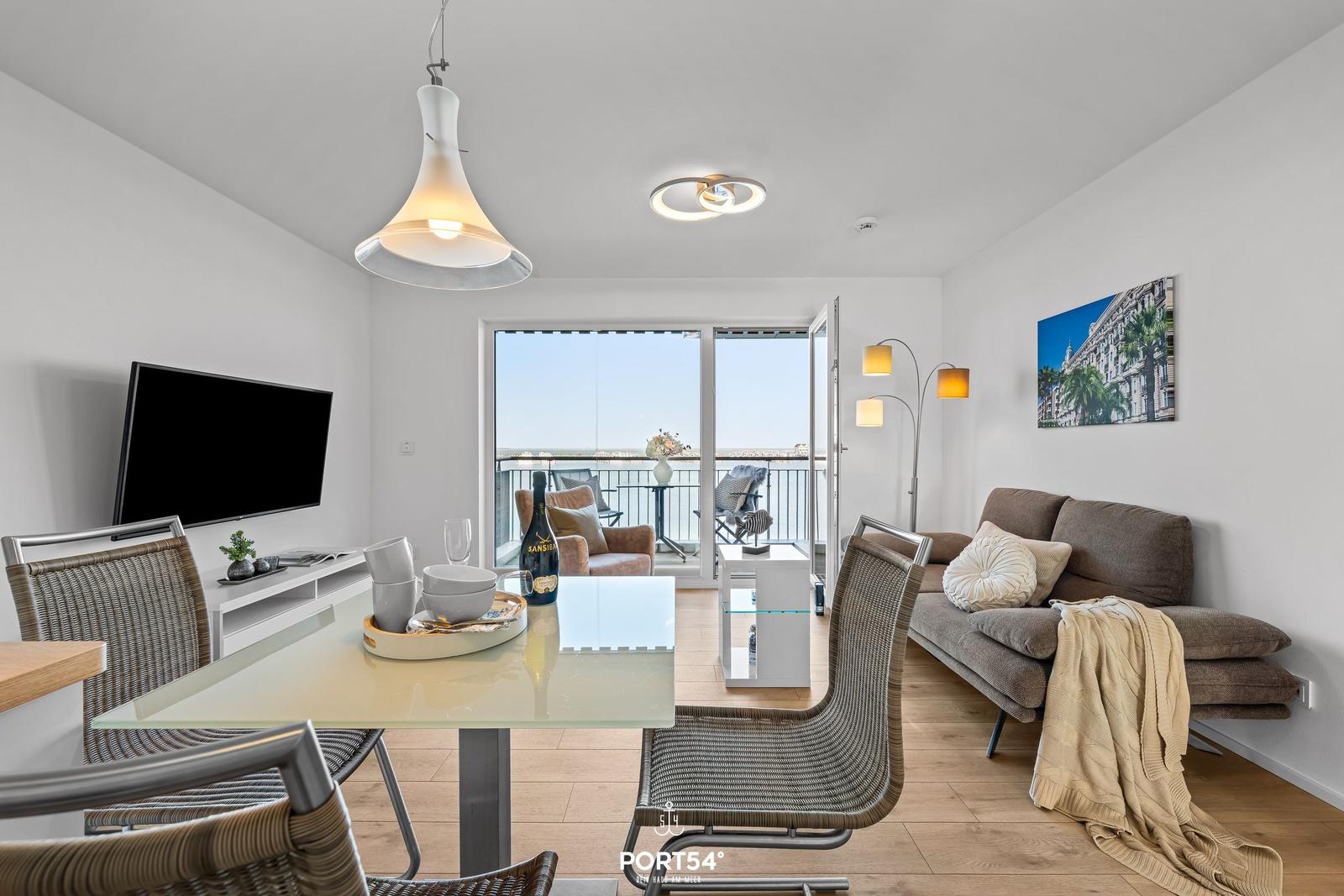 Wohn- und Essbereich mit Balkon, Sofa, Esstisch und Fernseher.