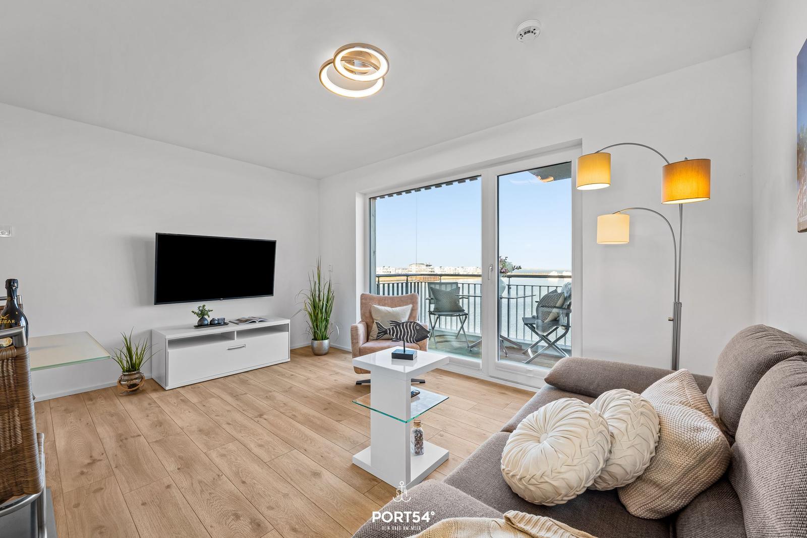Wohnzimmer mit Sofa, Fernseher und Balkonansicht.