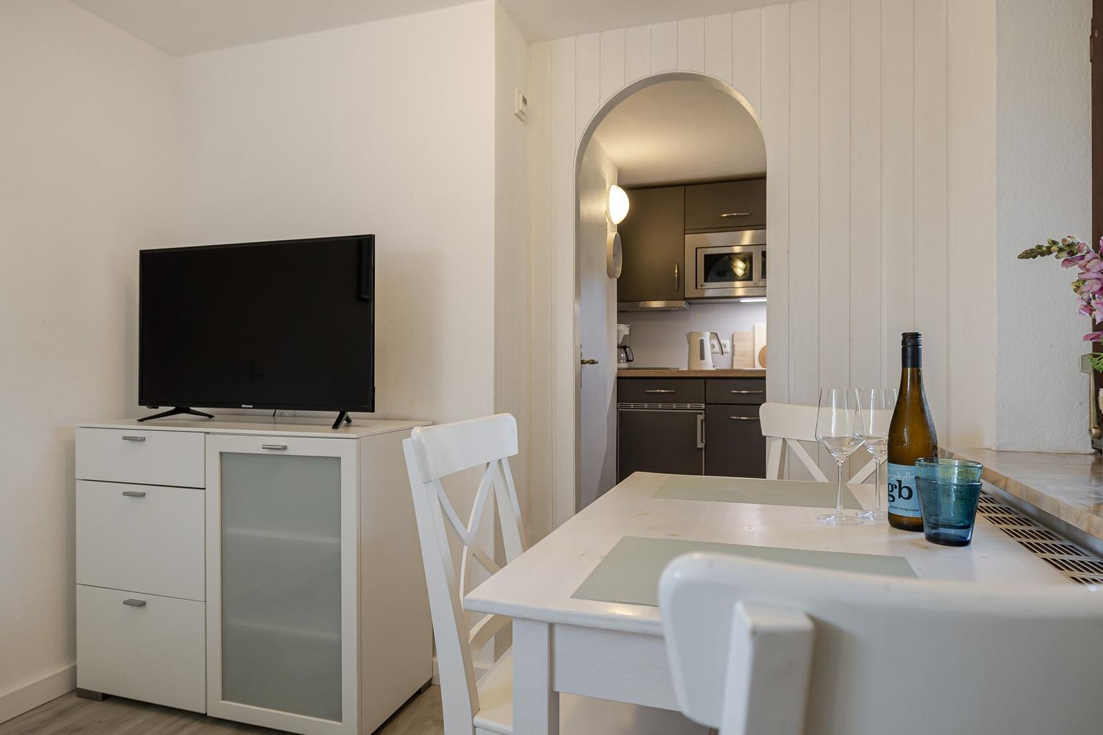 Essbereich mit Tisch, Stühlen und Fernseher. Durch Bogen Zugang zur Küche.