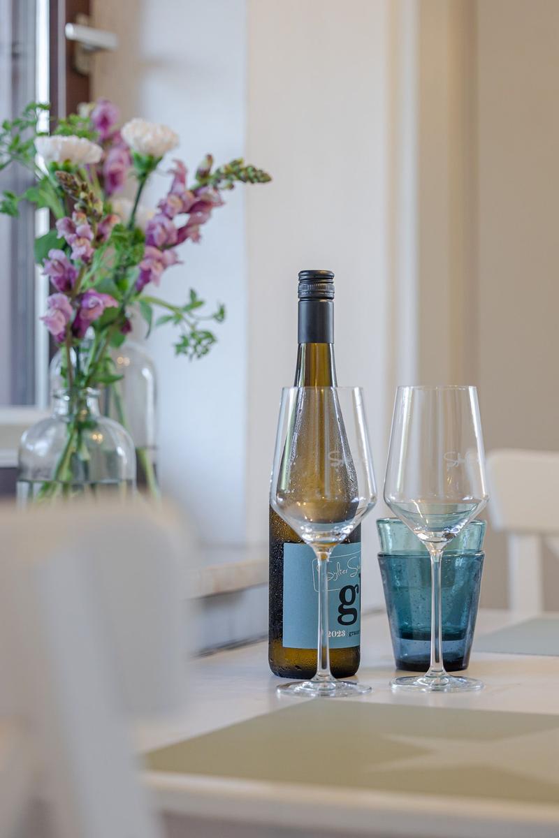 Weinflasche und Gläser auf Tisch neben Blumenarrangement.