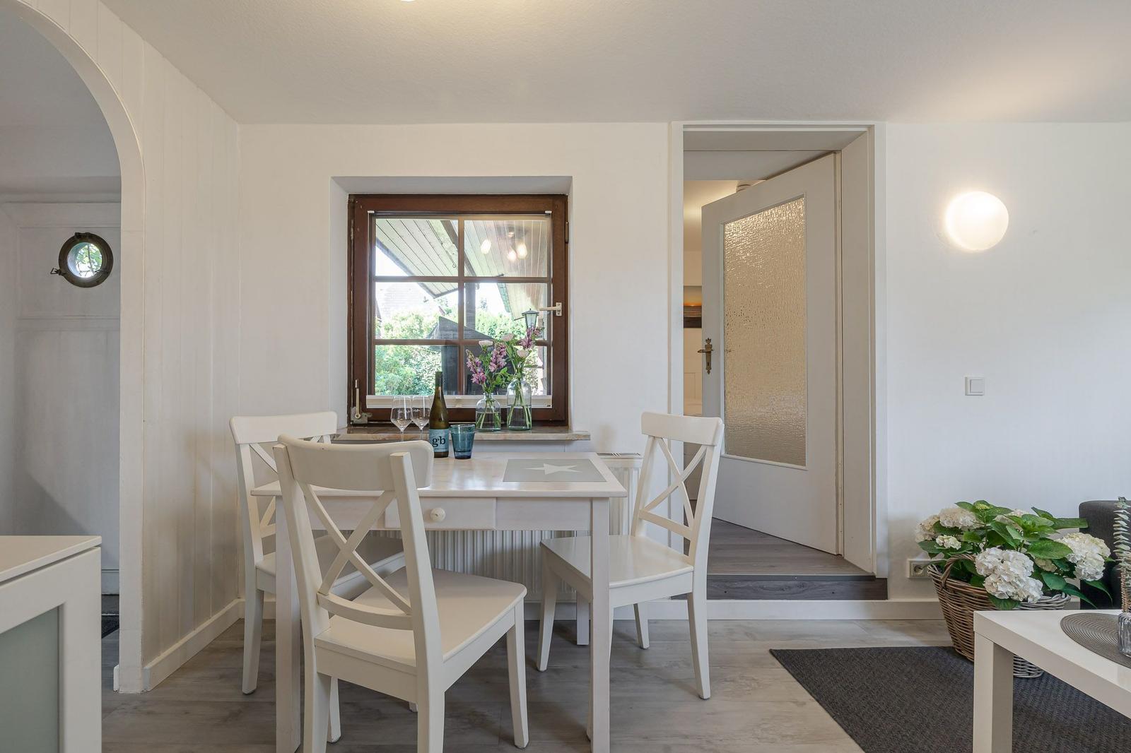 Esszimmer mit weißem Tisch und Stühlen, Fenster mit Blumen und Blick nach draußen.