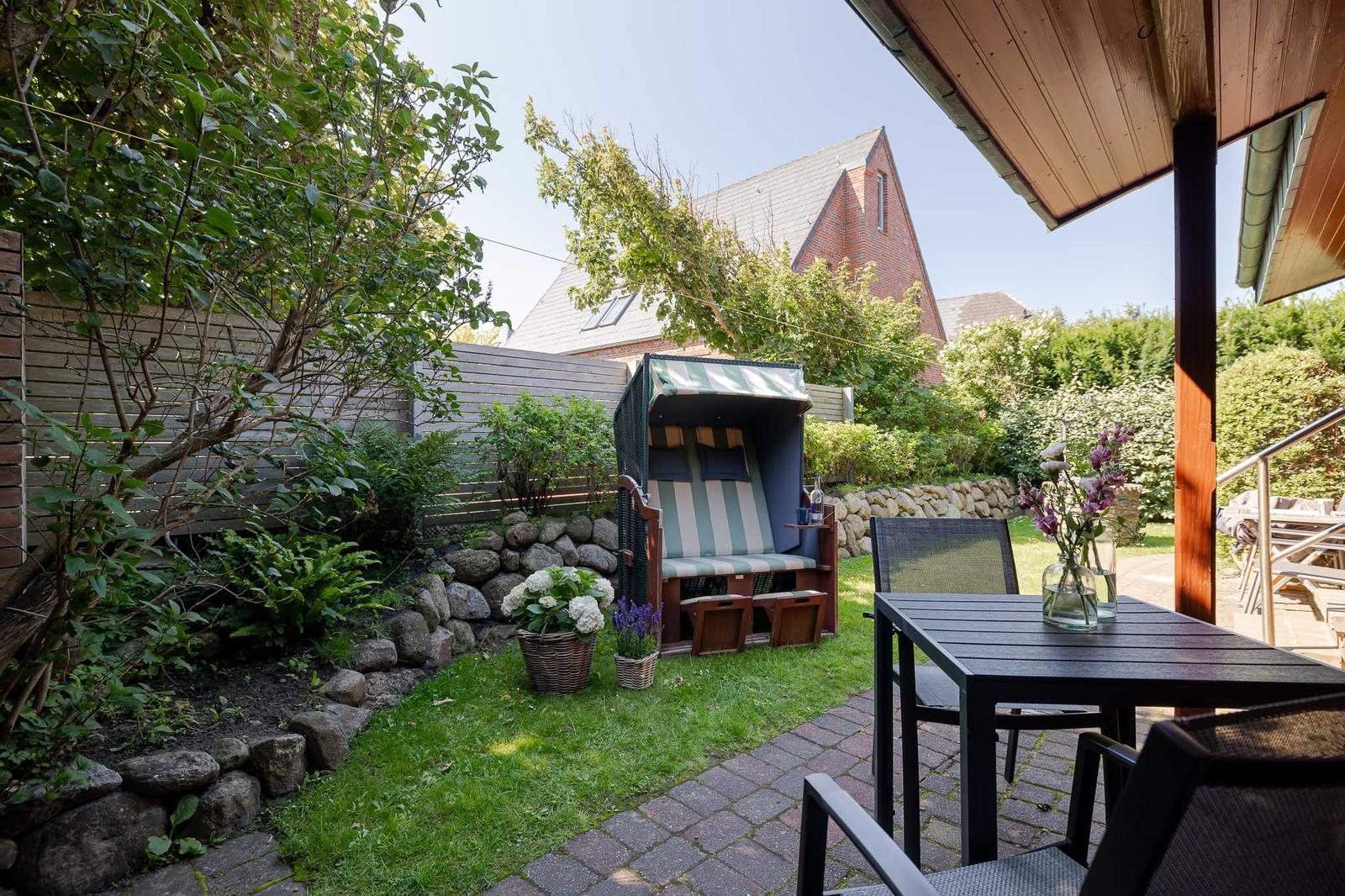 Terrasse mit Tisch, Stühlen und Strandkorb im Garten.