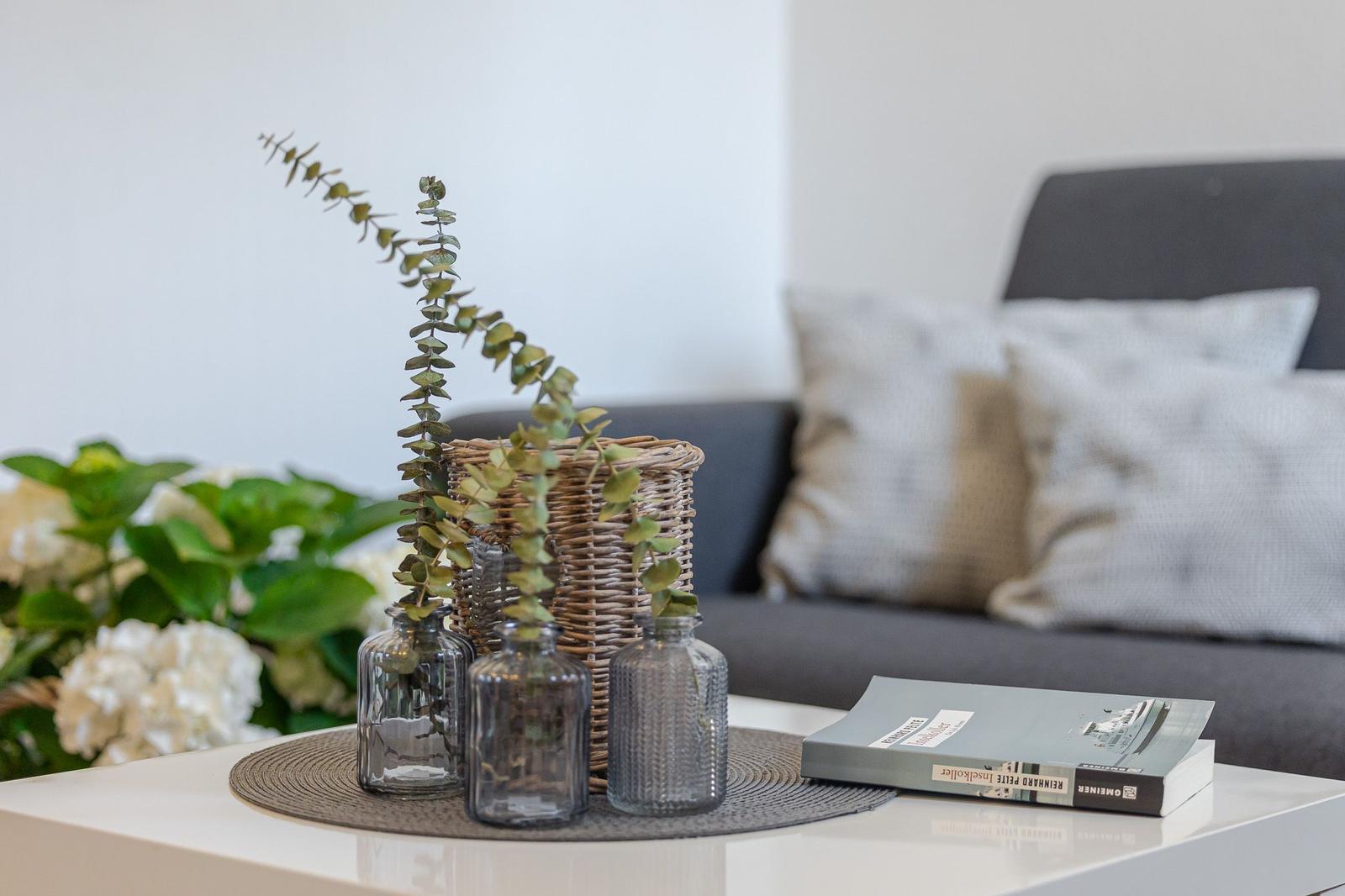 Tisch mit Vasen, Pflanzen und Buch vor Sofa