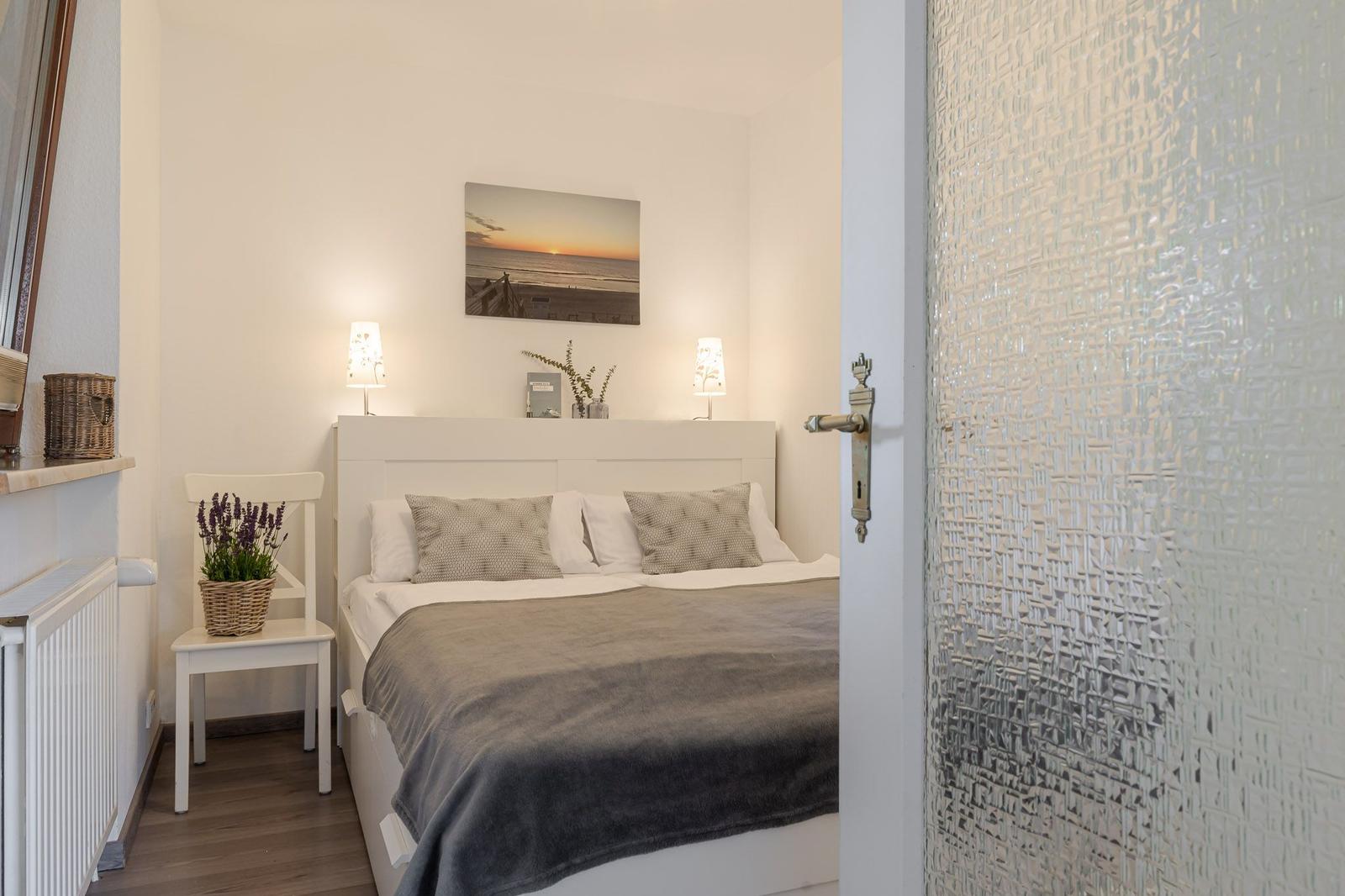 Schlafzimmer mit weißem Bett, Wandbild und Nachttischen.