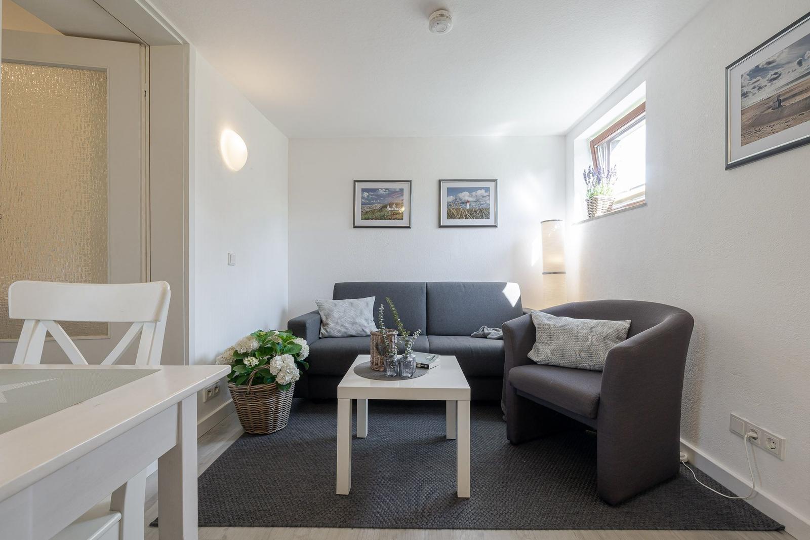 Wohnzimmer mit grauem Sofa, kleinem Tisch und Pflanzen.