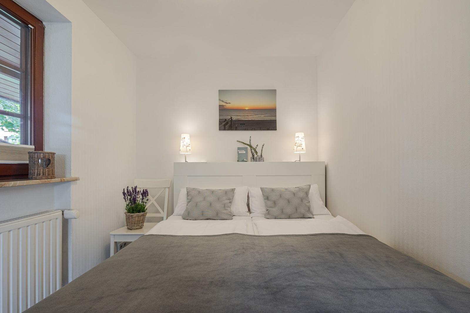 Schlafzimmer mit Bett, Nachttisch, Wandbild und Fenster.