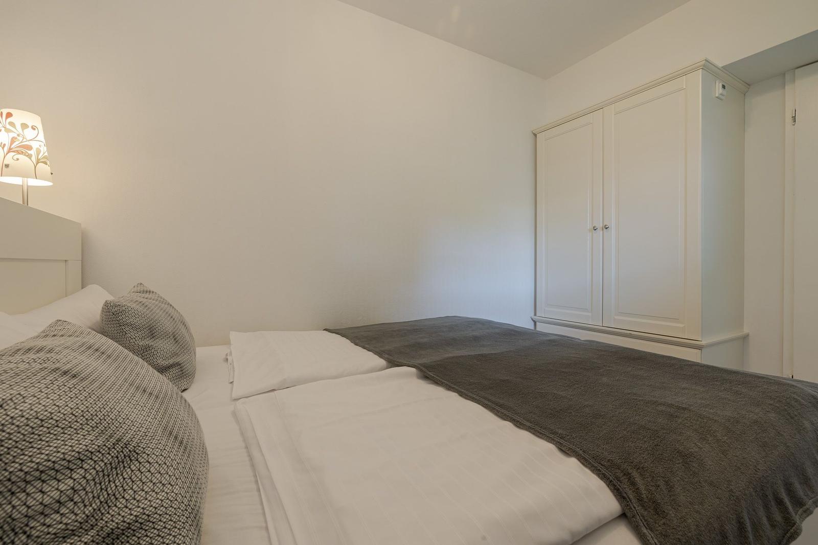 Schlafzimmer mit Bett, Kleiderschrank und Nachttischlampe.