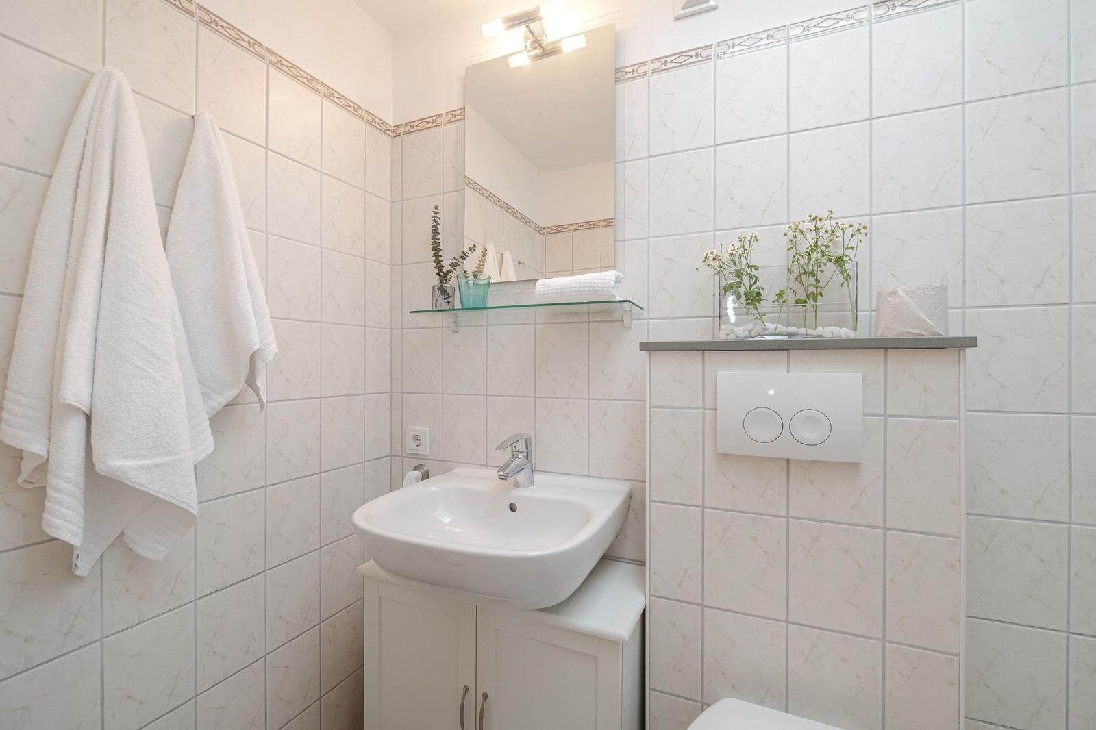 Badezimmer mit Waschbecken, Spiegel und Handtüchern an der Wand.