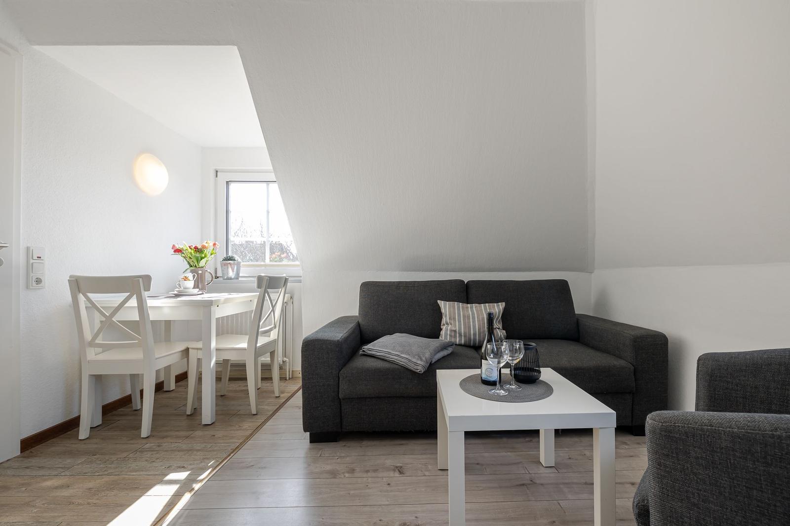 Wohn- und Essbereich mit grauem Sofa, weißem Tisch und Holzboden.