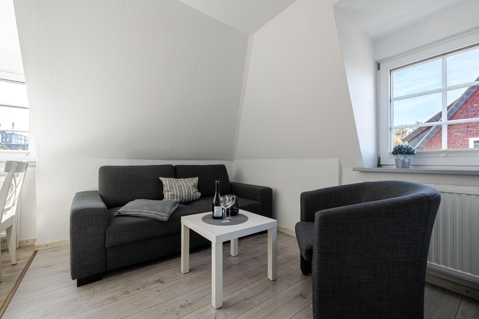 Wohnzimmer mit Sofa, Sessel und Tisch unter Dachschrägen.