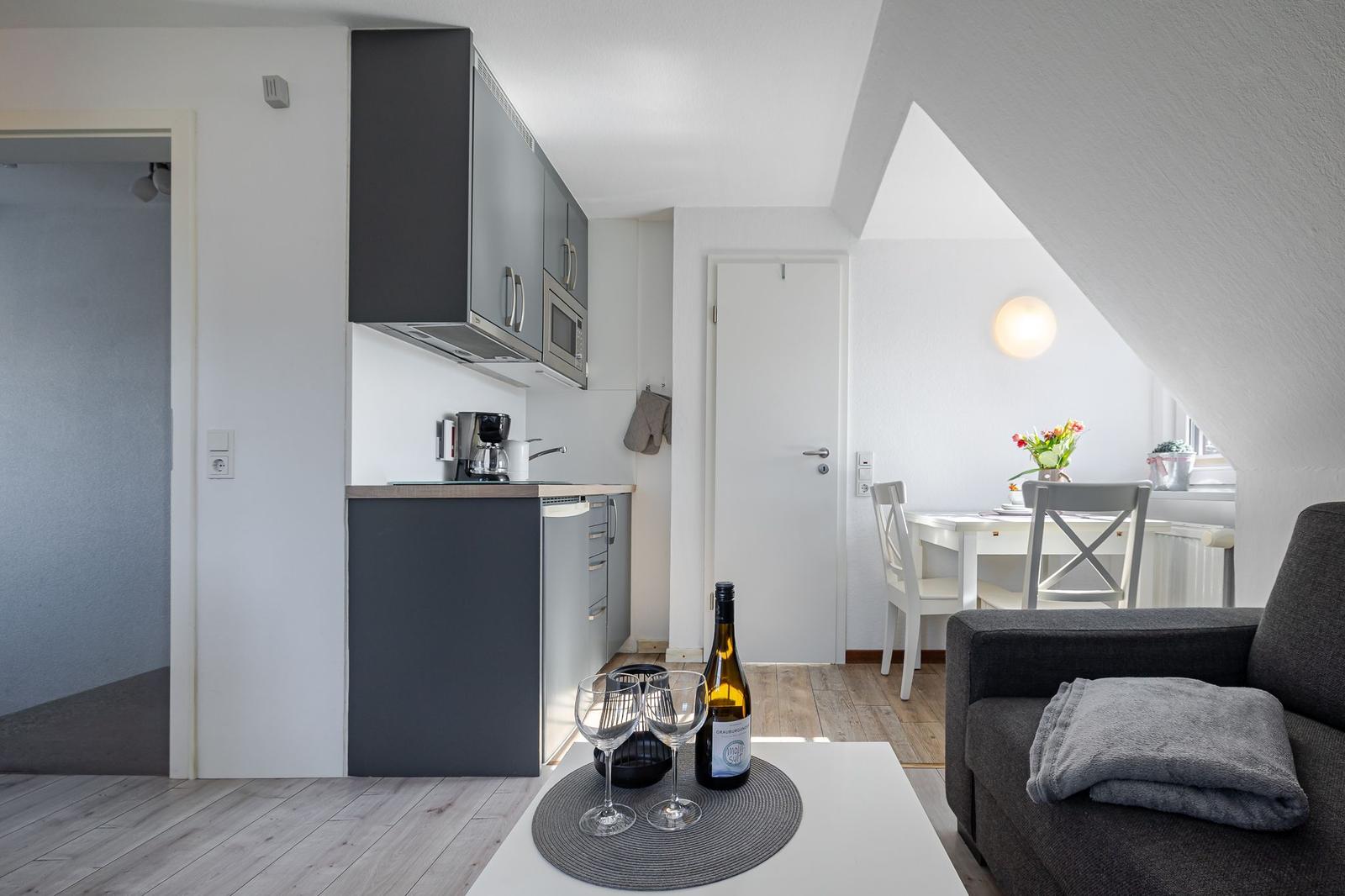 Küche, Essbereich und Wohnbereich mit dunklem Sofa und Wein auf Tisch.