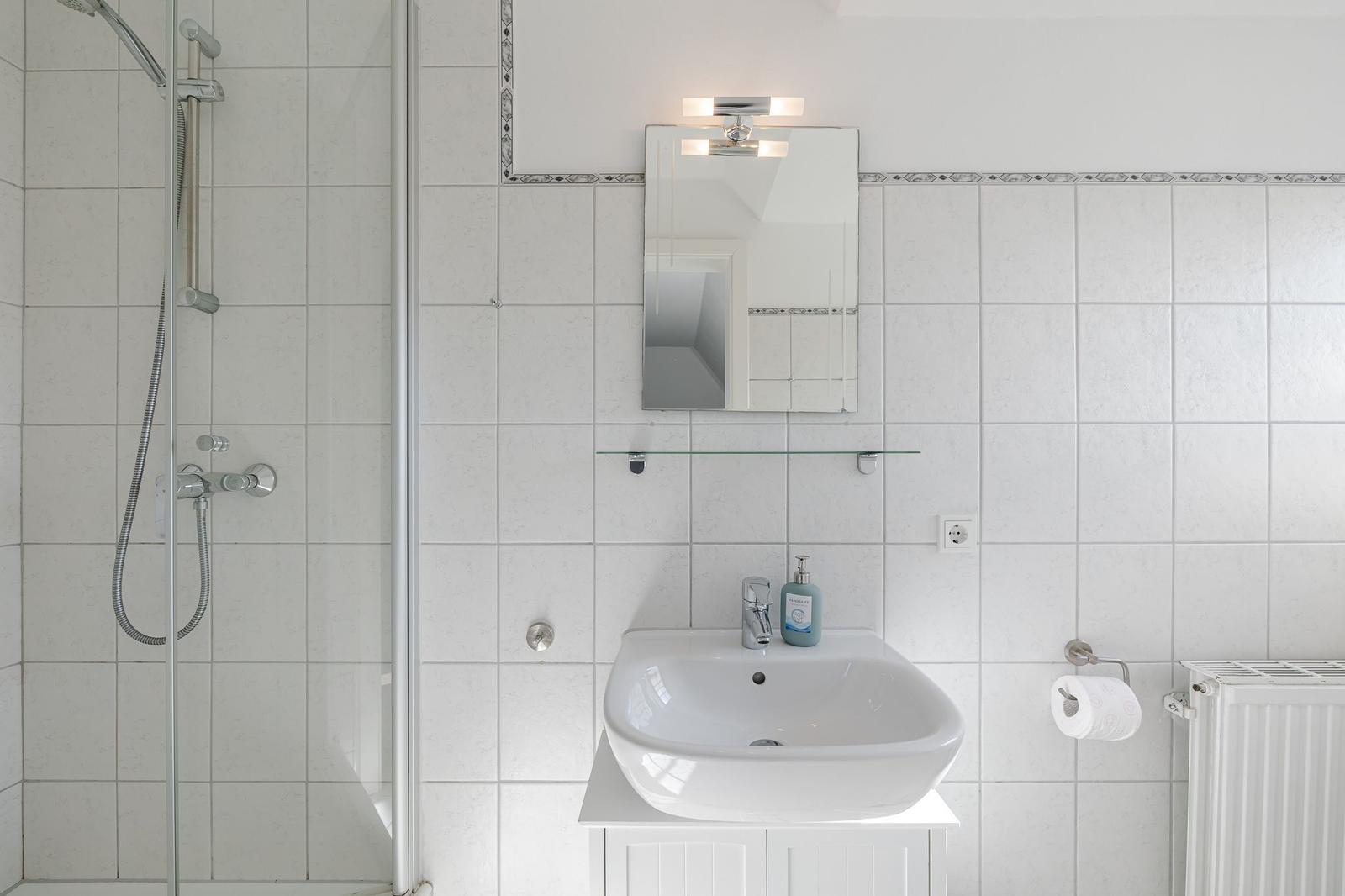 Badezimmer mit Dusche, Waschbecken und Spiegel