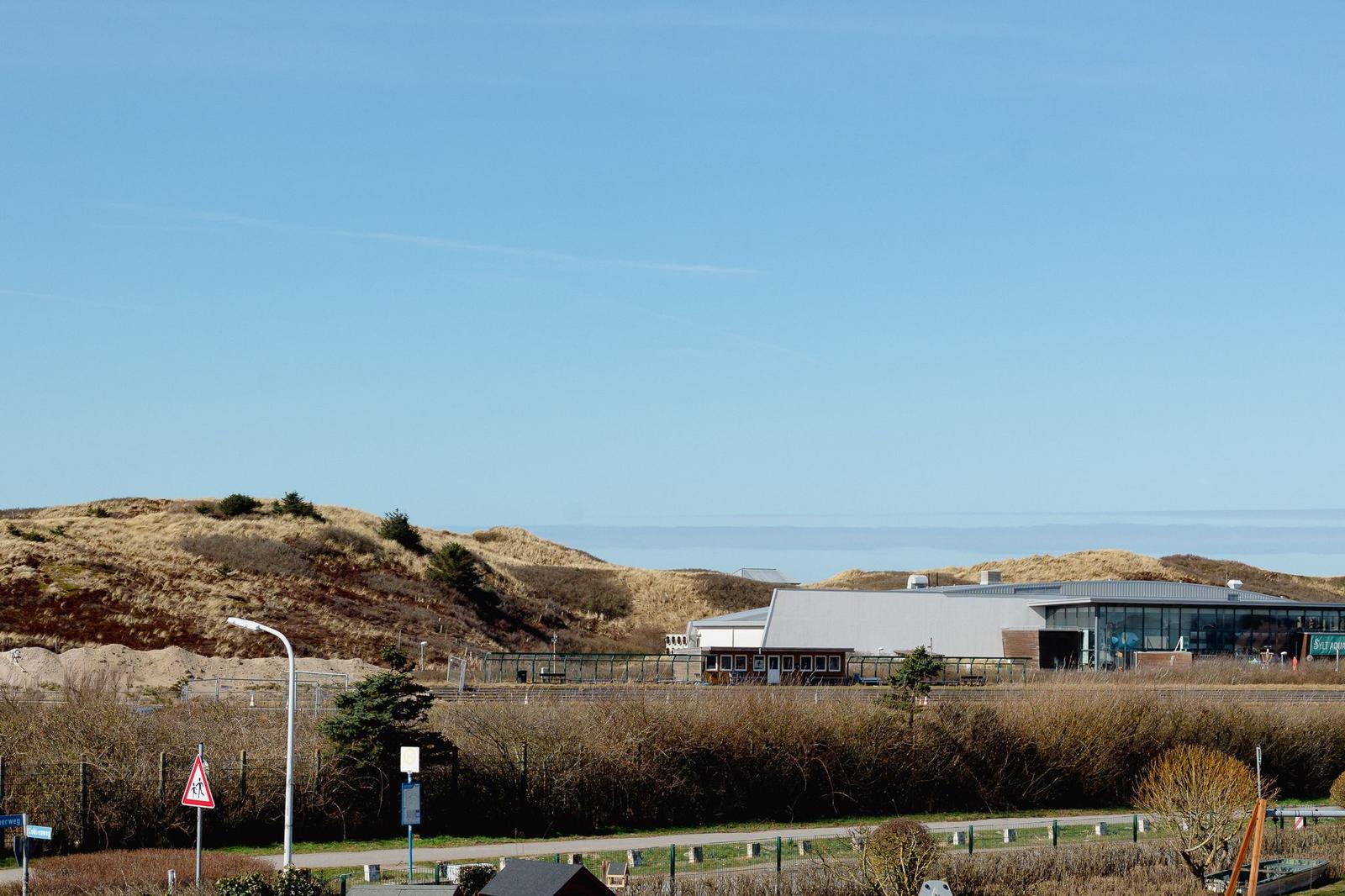 Moderne Gebäude mit Glasfassade zwischen Dünen und Strand.
