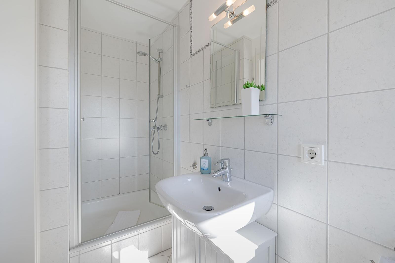 Badezimmer mit Dusche, Waschbecken und Spiegel.