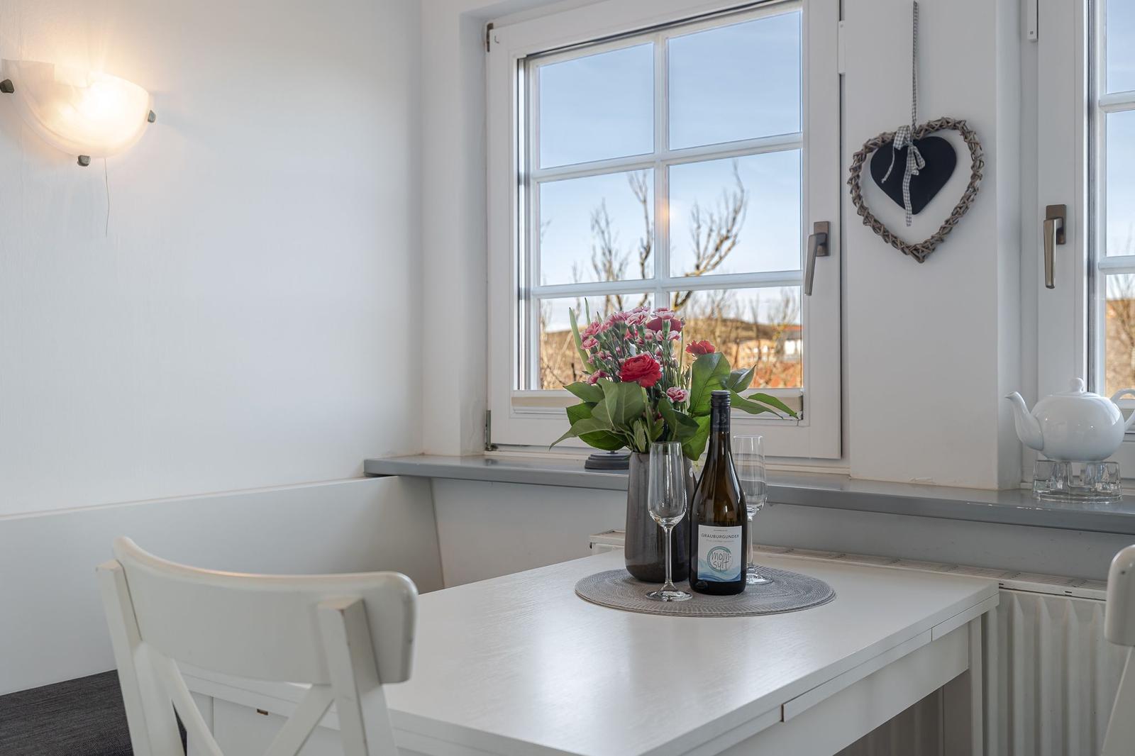 Tisch mit Blumen, Wein und Teekanne am Fenster