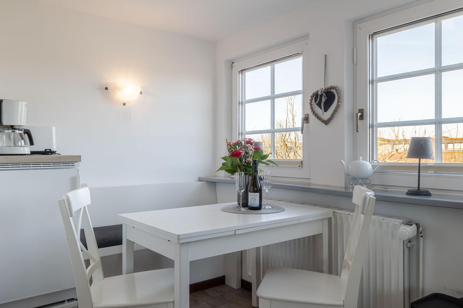 Essbereich mit weißem Tisch und Stühlen, Fenster mit Blick nach draußen und Blumen auf dem Tisch.